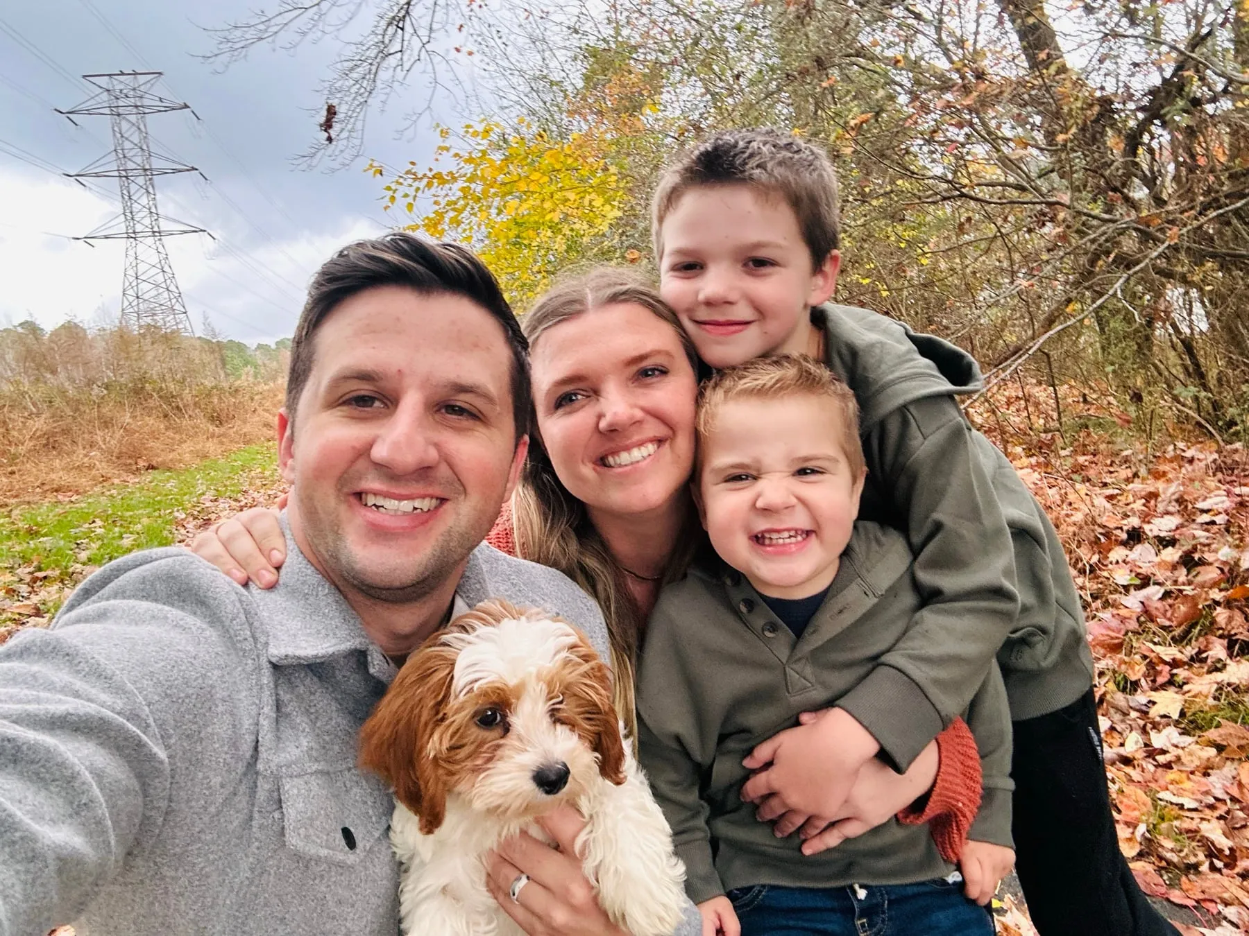 Mom, Dad, our two boys and our puppy squeezed into a selfie among fall leaves