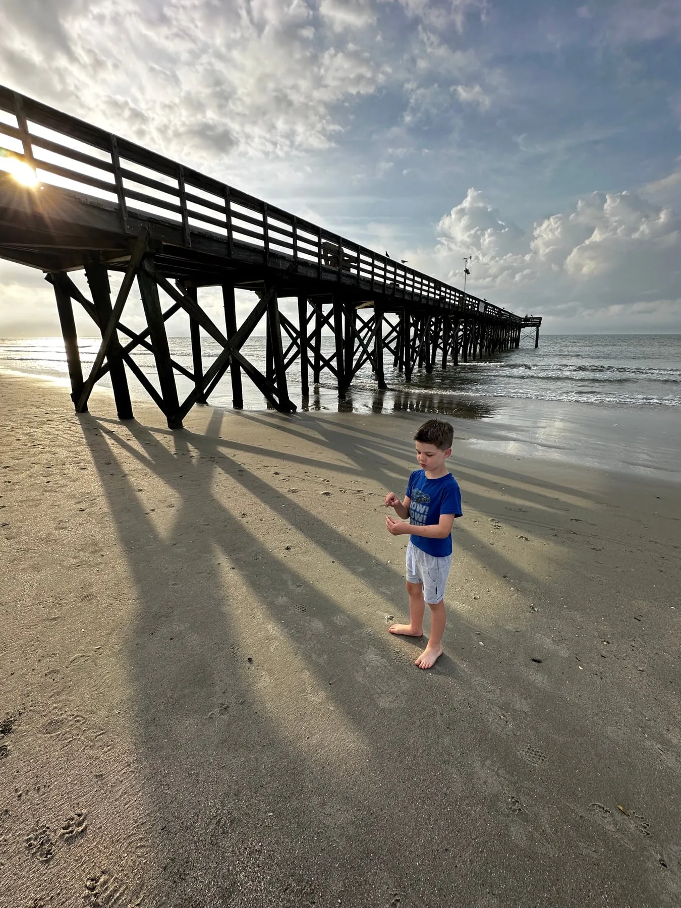 A little boy standing in the long shadows under a beach pier in South Carolina